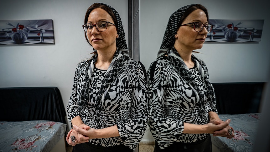 A woman in a black and white graphic top and headscarf stands next to a mirror so you can see her reflection
