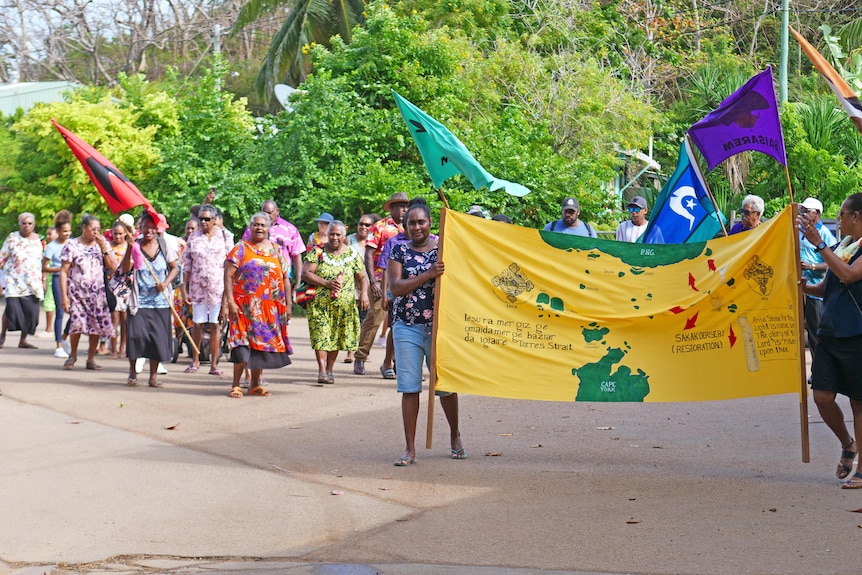 A group of Torres Strait Islanders with flags walk through the street.