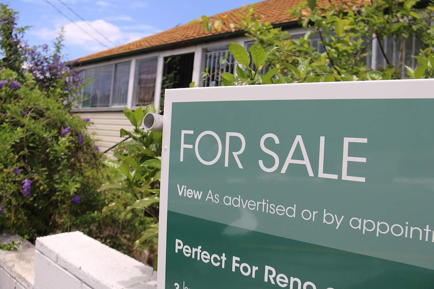 For sale sign on Queenslander-style house that needs renovating in a street in Brisbane.