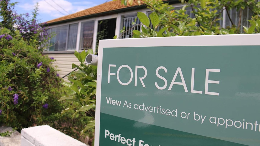 For sale sign on Queenslander-style house that needs renovating in a street in Brisbane.