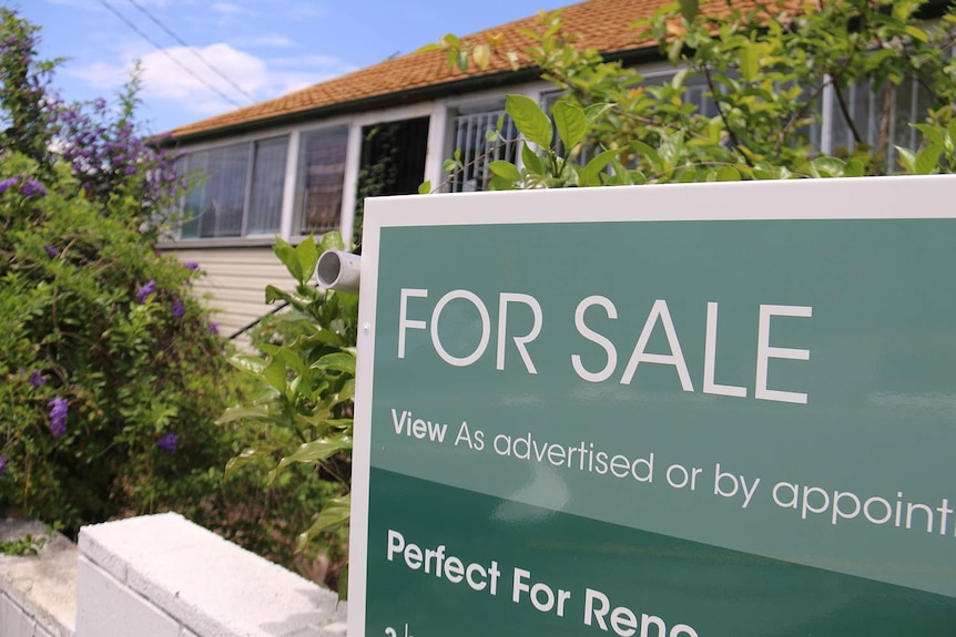 For sale sign on Queenslander-style house that needs renovating in a street.