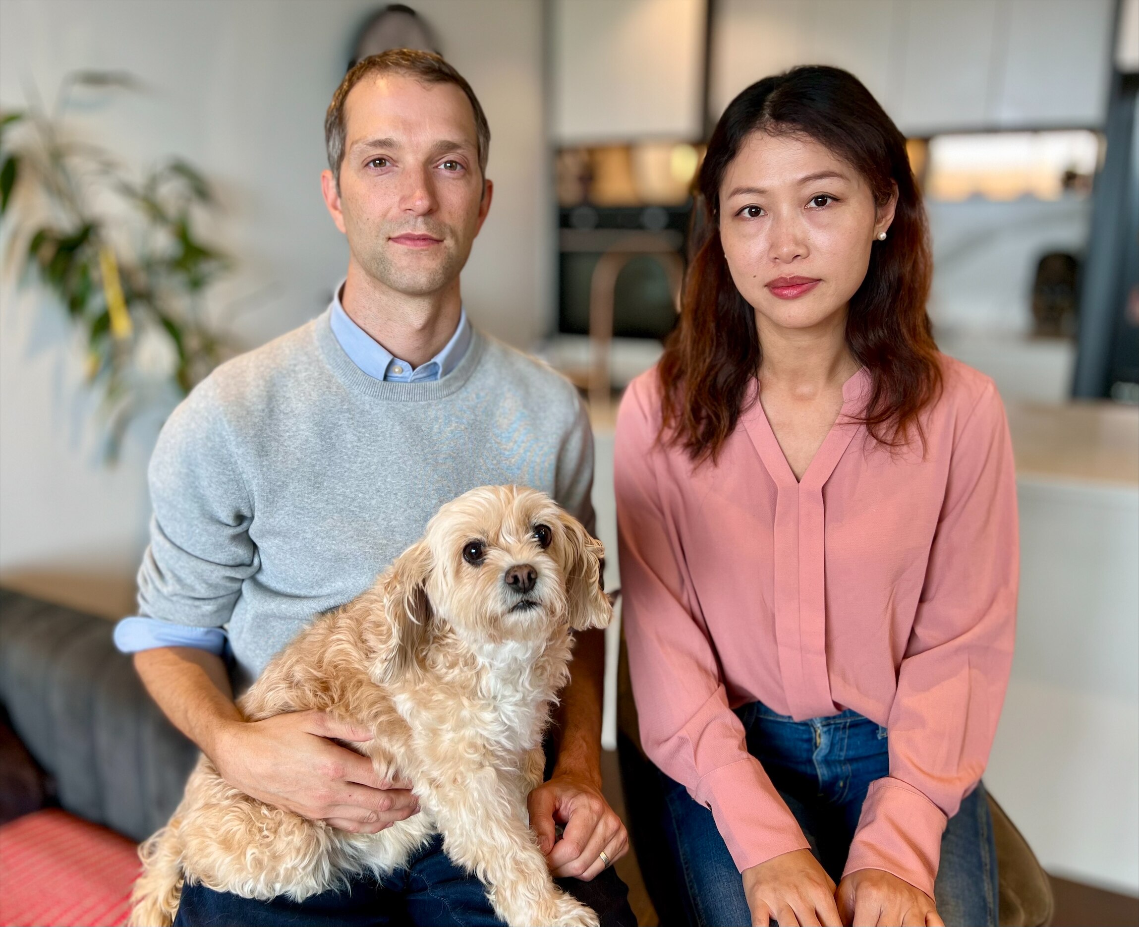 A man in a grey jumper and a woman in a pink shirt sit together with a dog.