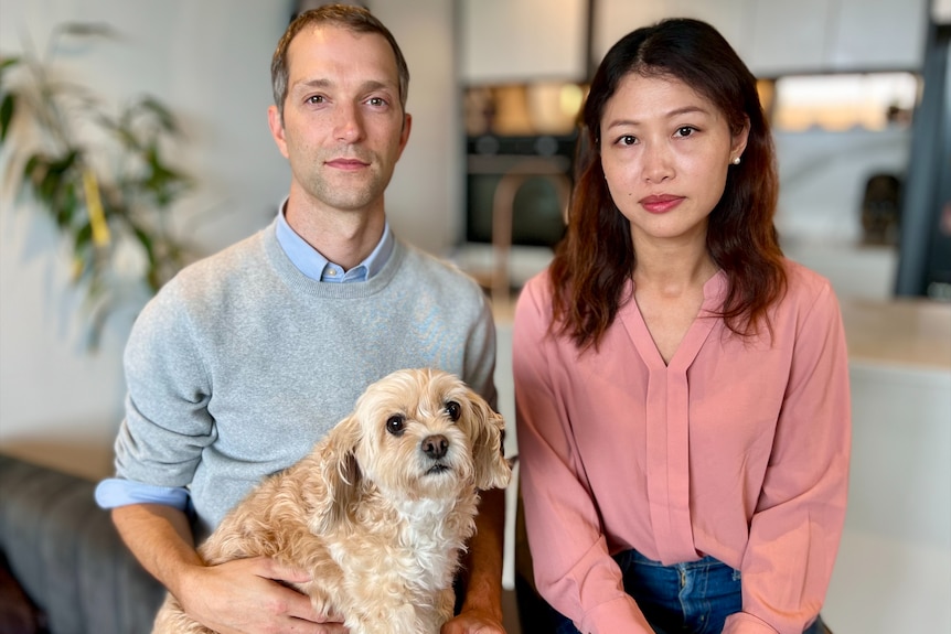 A man in a grey jumper and a woman in a pink shirt sit together with a dog.