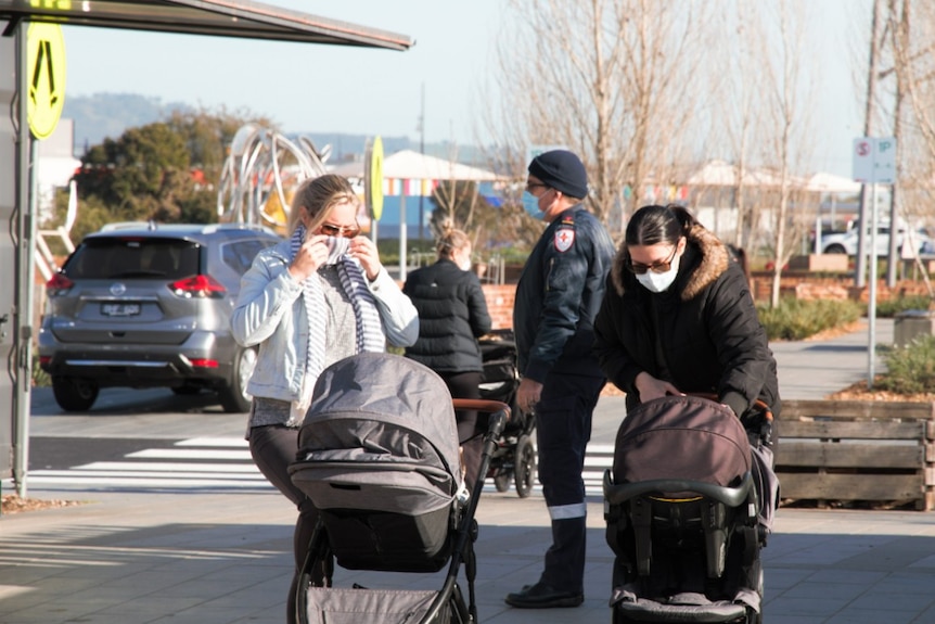 Two women wearing face coverings look down at their prams on a footpath in Wodonga.