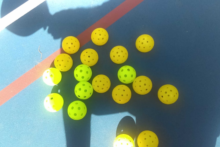 Perforated yellow plastic balls lying on a court.