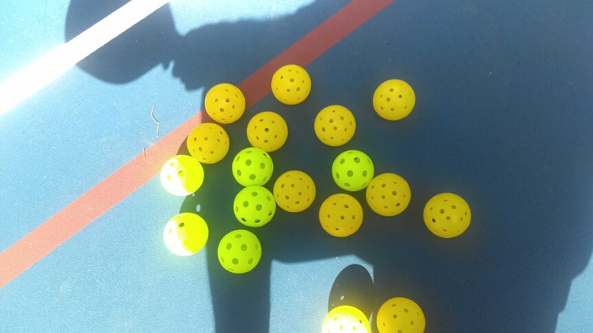 Perforated yellow plastic balls lying on a court.