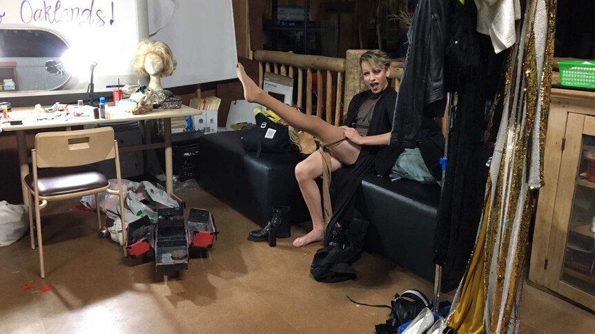 Elijah Mortlock rolls up stockings in change room, pointing his toe. He's surrounded  by clothes and makeup