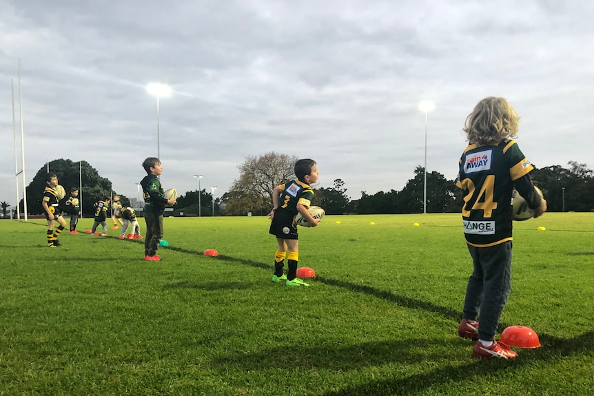 Young boys line up with rugby league footballs.