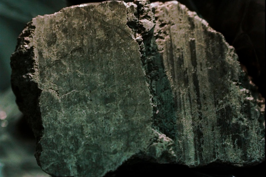 A close up of a hand in a glove holding the meteorite.