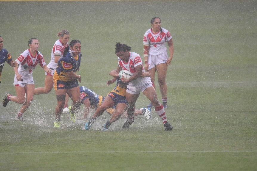 Una mujer carga contra los defensores en un partido de la liga de rugby jugado bajo una lluvia torrencial. 