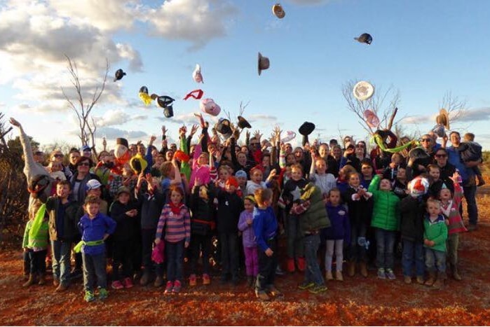 A large group of parents and school students throwing their hats in the air after a school camp.