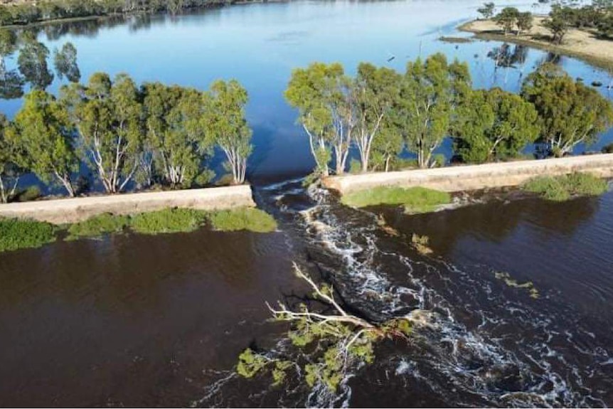 A break in a levee with water surrounding the levee and rushing through the break