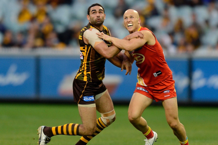 Two AFL players wrestle as they wait to mark a ball.