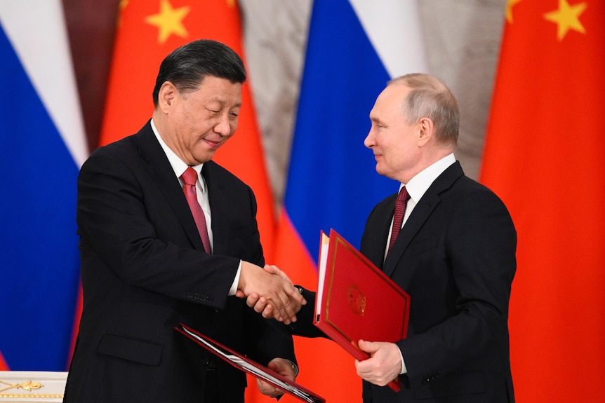 习近平（左）和普京在中俄两国国旗的背景前握手。