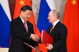 习近平（左）和普京在中俄两国国旗的背景前握手。