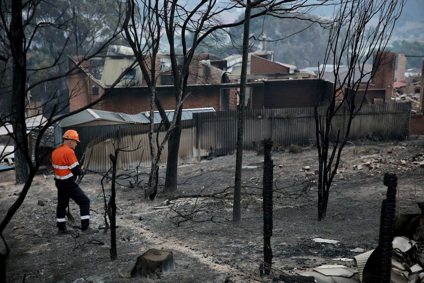 A worker in high vis clothing stands next to a razed house.