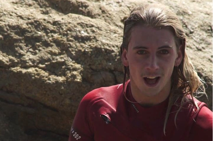 Bodyboarder Noah Symmans in a wetsuit with rocks in the background.