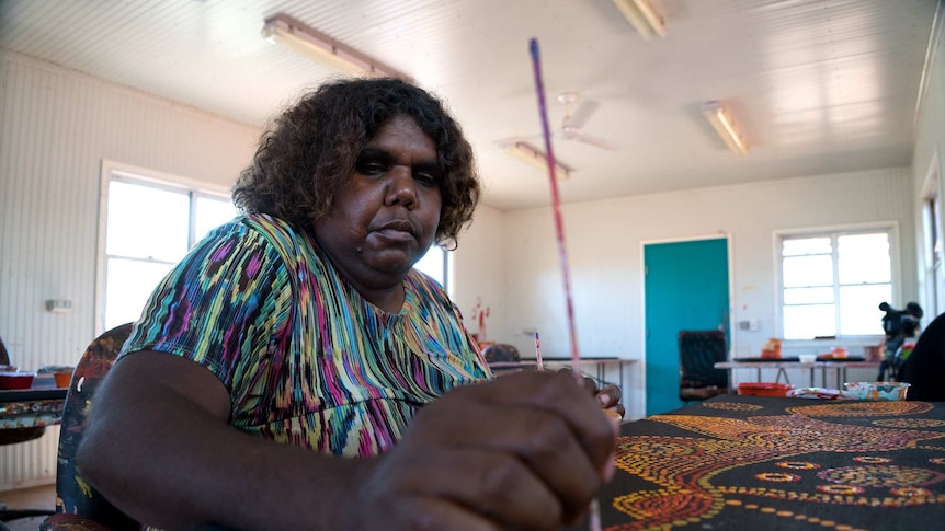 An Indigenous woman paints spots onto a painting in a art workshop.