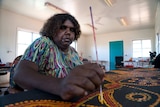 An Indigenous woman paints spots onto a painting in a art workshop.