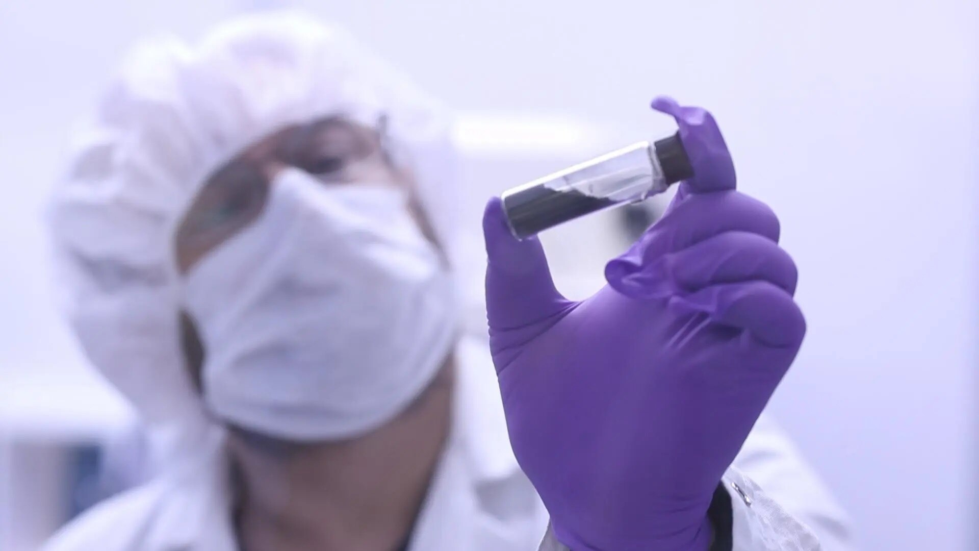 A masked scientist holds a glass vial containing rock grains from the asteroid Bennu