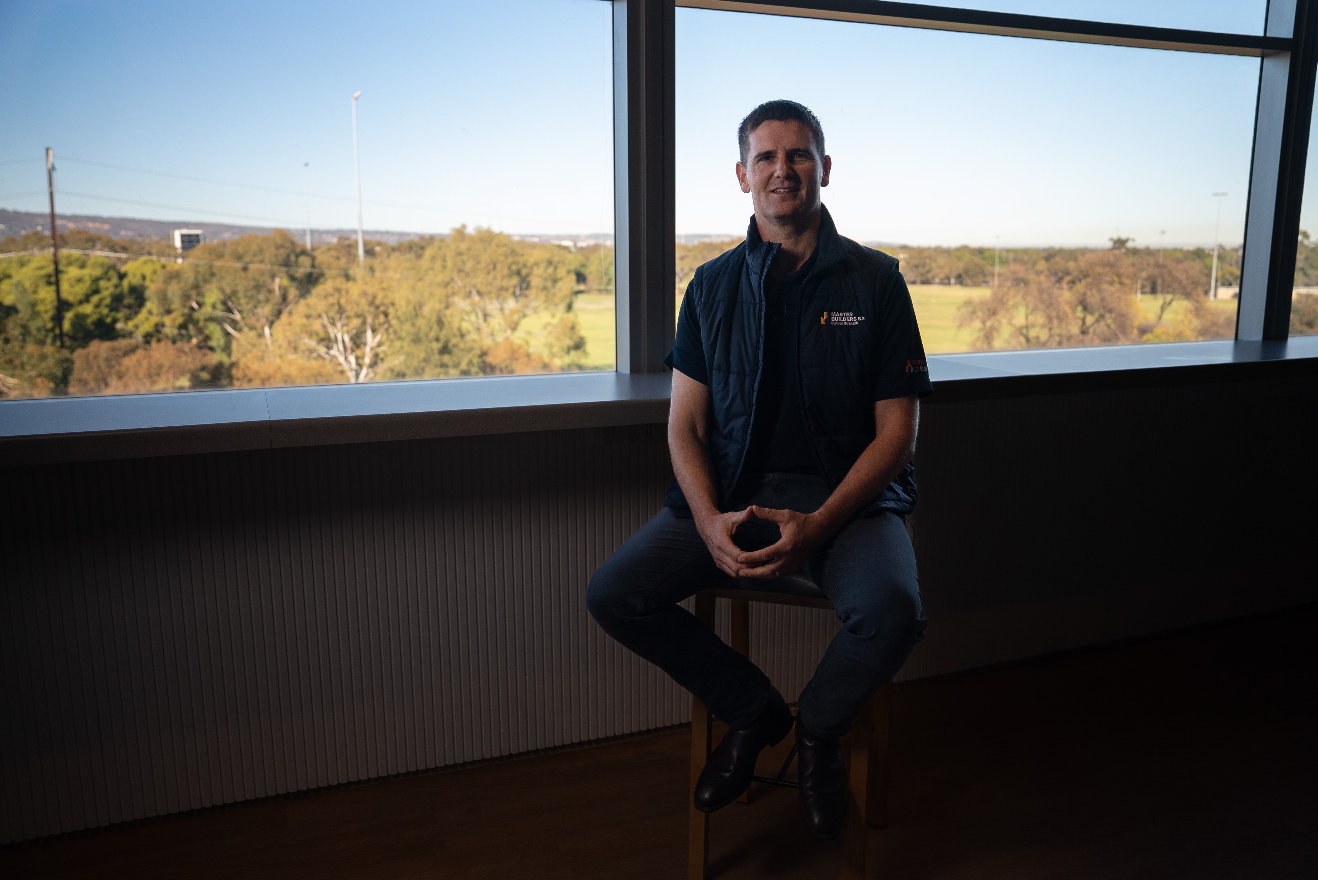 A man sits on a stool in front of a large window.