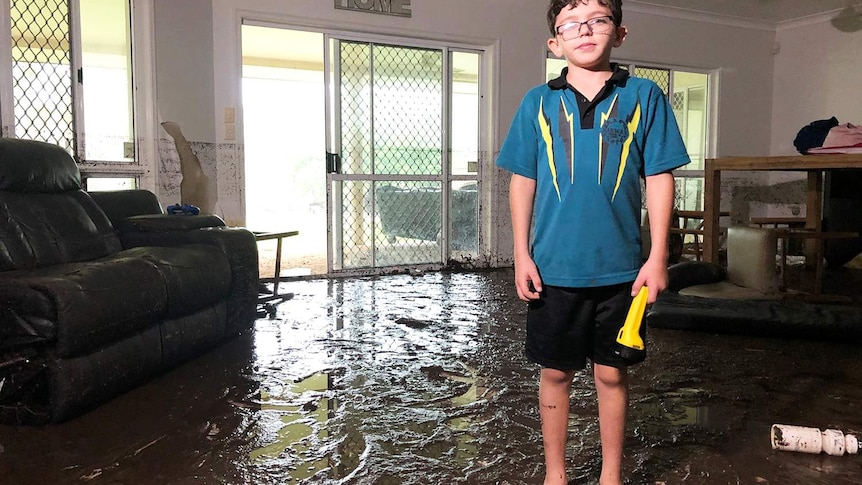 Ten-year-old Ky Brennan stands in water in his loungeroom of his flood-ravaged house in Bluewater