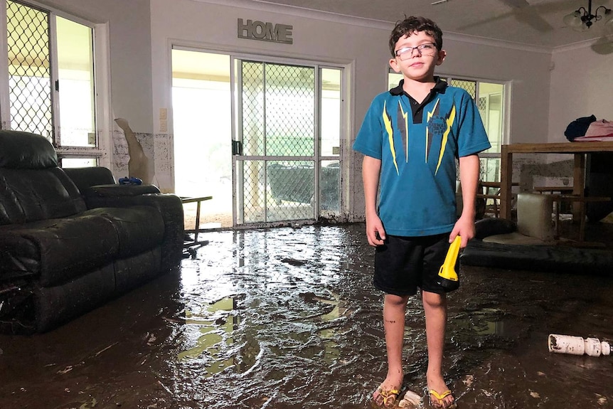 Ten-year-old Ky Brennan stands in water in his loungeroom of his flood-ravaged house in Bluewater