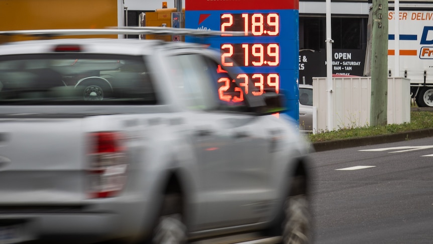 A blurred car driving on the highway with petrol prices showing behind it