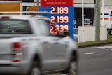 A blurred car driving on the highway with petrol prices showing behind it