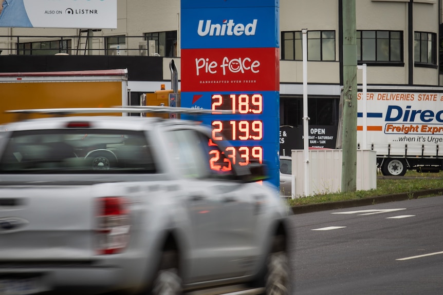 O mașină discretă care rulează pe autostradă și în spatele ei arătând prețul benzinei