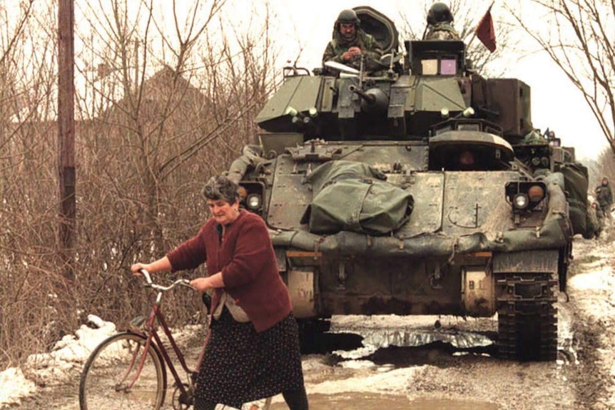 Woman wheels bike in front of US armoured personnel carrier in Bosnia
