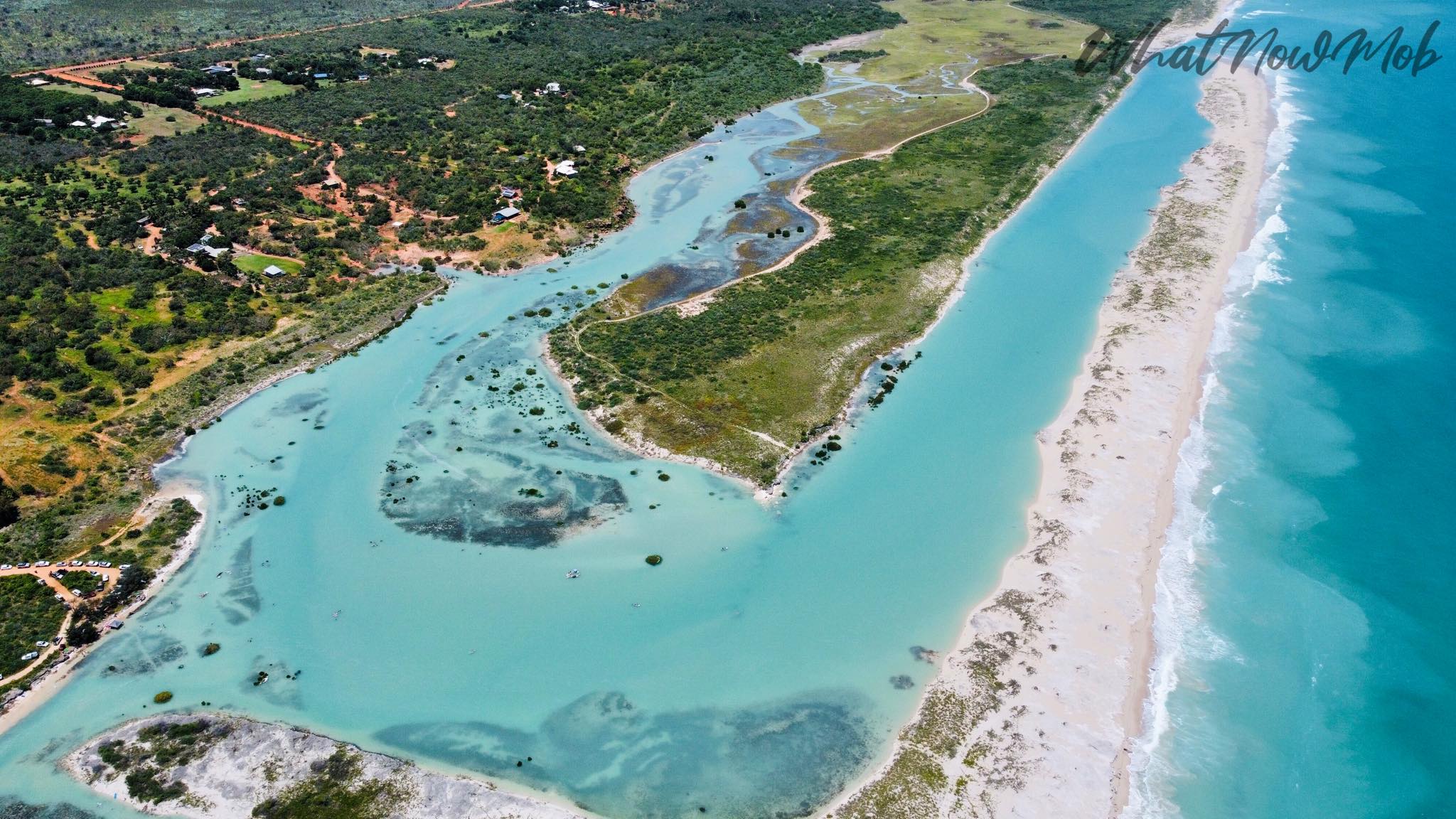 Bright blue ocean and a white sandbar against green bushland 