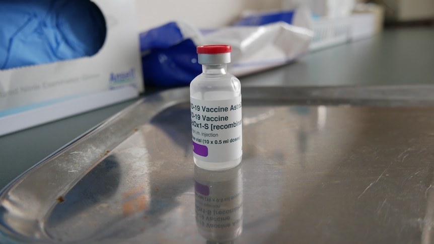 A clear glass vial with a label on a silver tray, with medical gloves and tissues behind