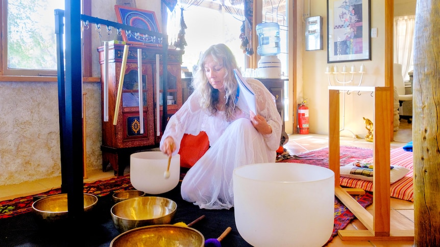 Woman in light-filled room playing sound bowls.