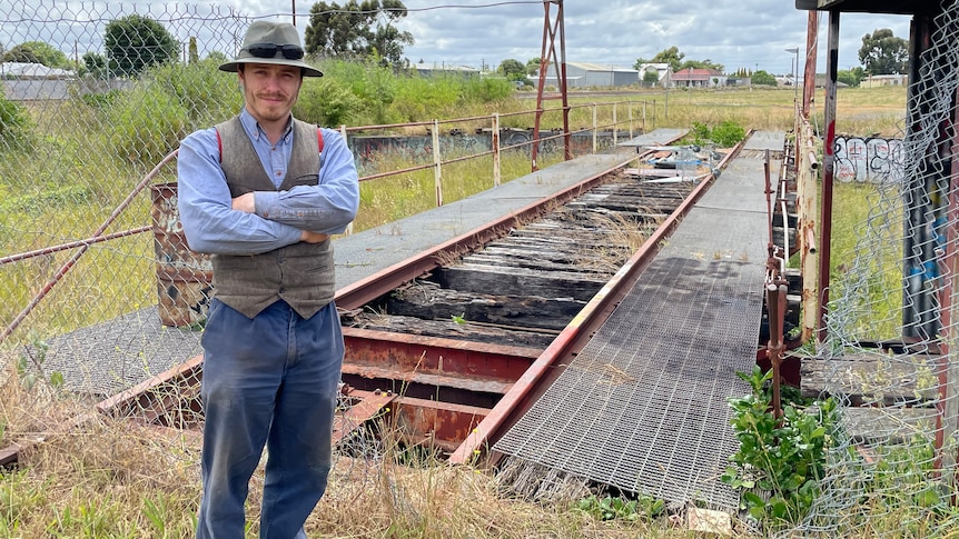 A man stands at an old rail platform with his arms folded