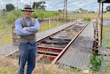 A man stands at an old rail platform with his arms folded