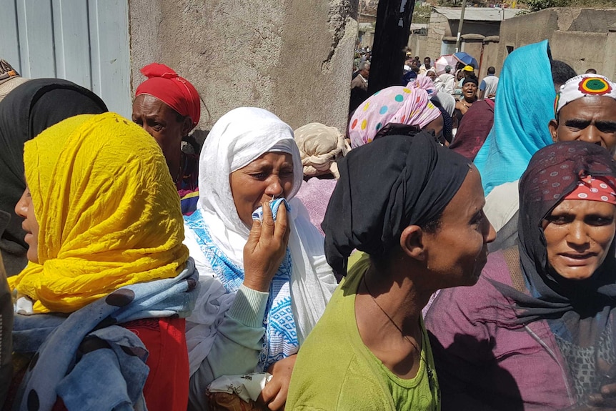 People crying and standing together. One woman holds her scarf to her mouth as she cries.