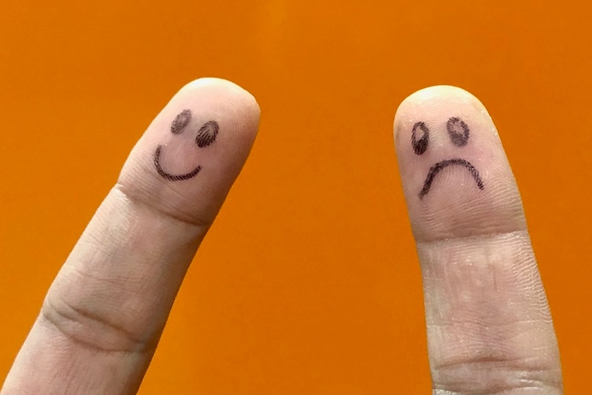 Two index fingers with a happy and sad face drawn on, with orange background.