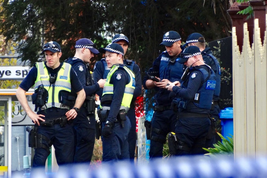 Seven police officers stand in front of apartments in Brighton the morning after a siege.