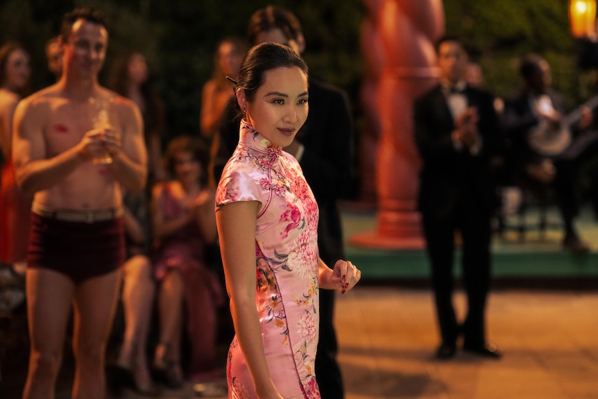 Li Jun Li usa un vestido rosa y sonríe mientras lleva su mano en un fotograma de la película Babylon.
