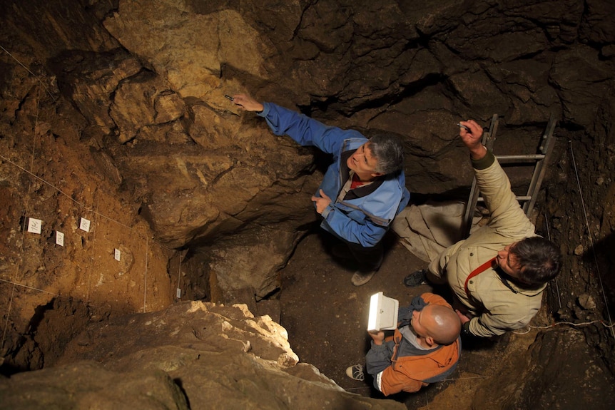 Three men stand in a deep hole