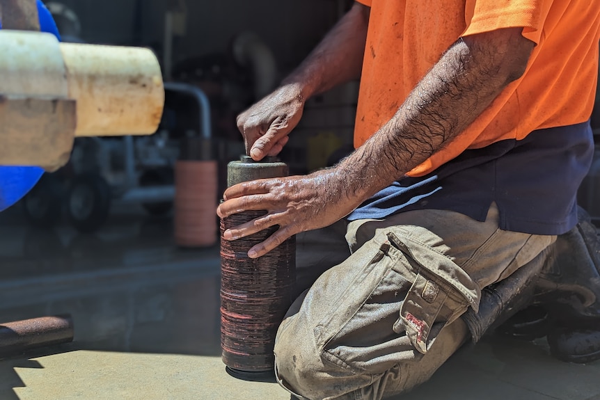 Sikh farmer Mintu's hands cleaning an irrigation filter, he wears a fluoro orange shirt and grey cargo pants.