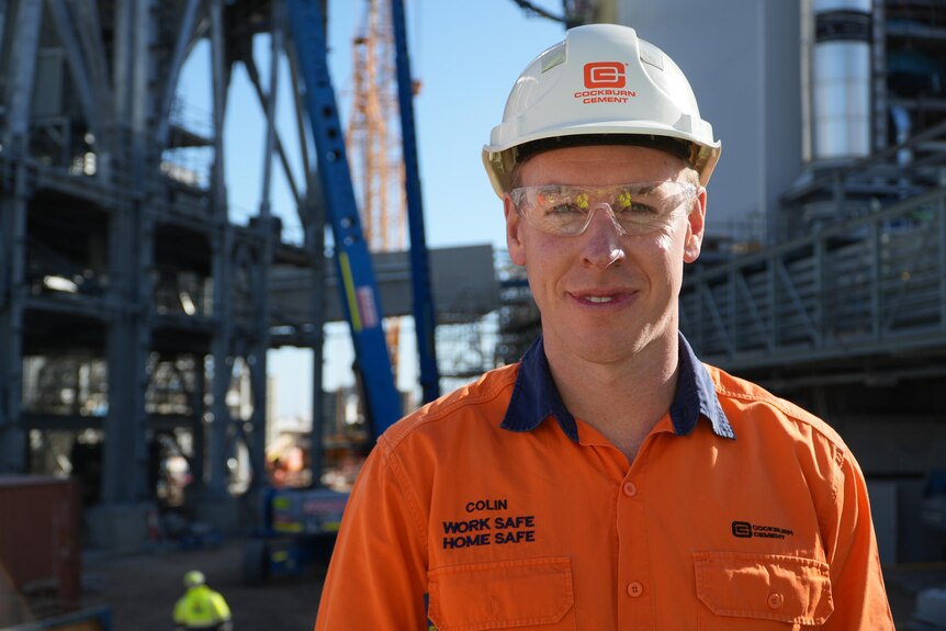 A man named Colin Powers wears high-vis gear and a hard hat.
