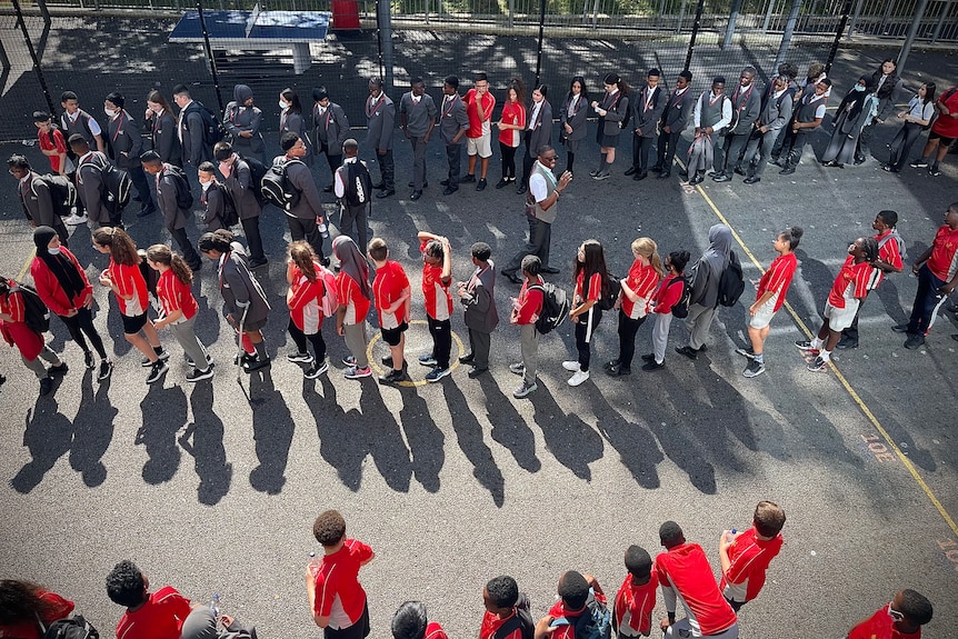An aerial shot of schoolkids lining up in a playground.