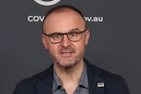 A man in glasses and a suit speaks at a podium.