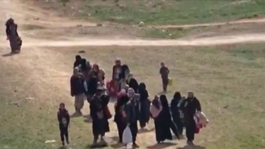 Civilians flee on foot through open ground from fighting near Baghouz.