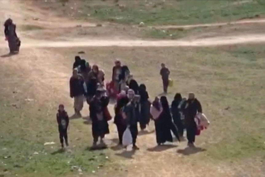 Civilians flee on foot through open ground from fighting near Baghouz.