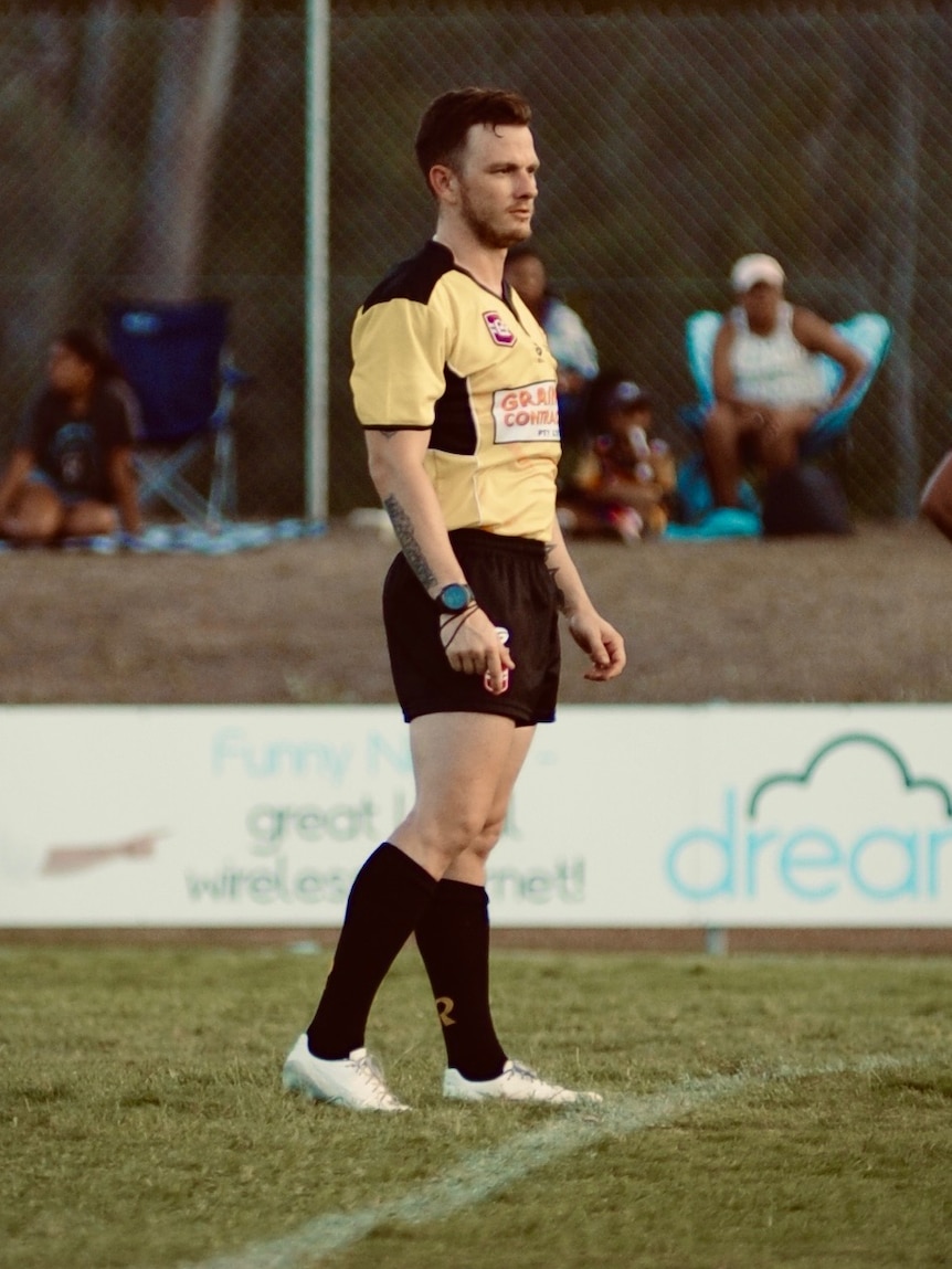 A man standing on the sidelines of a grass field