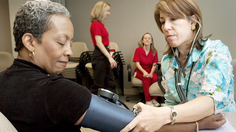 Woman receives blood pressure check by health professional in floral scrubs.