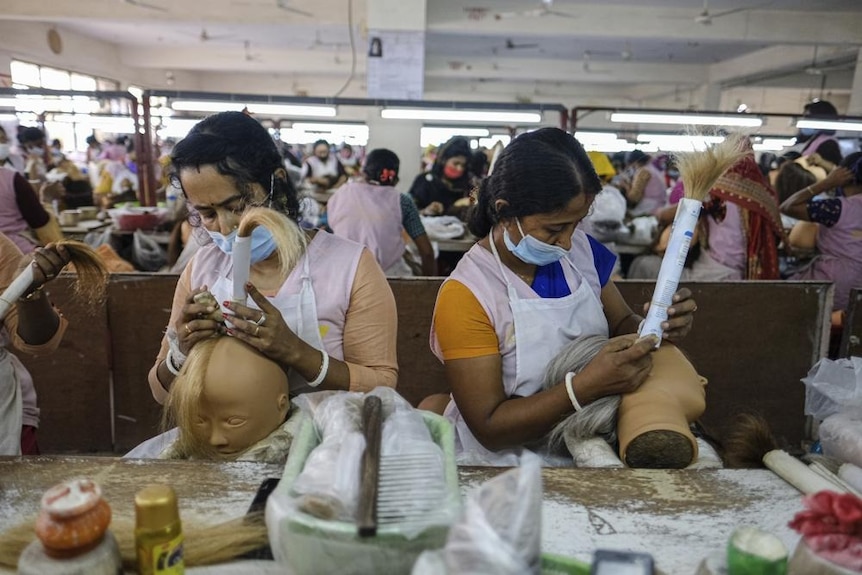 Две женщины в масках надевают волосы на манекены на фабрике. 